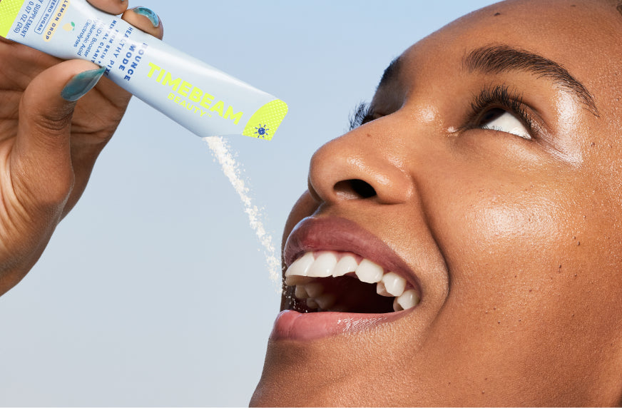 A woman tilting the contents of an open pouch of TIMEBEAM supplements into her mouth.