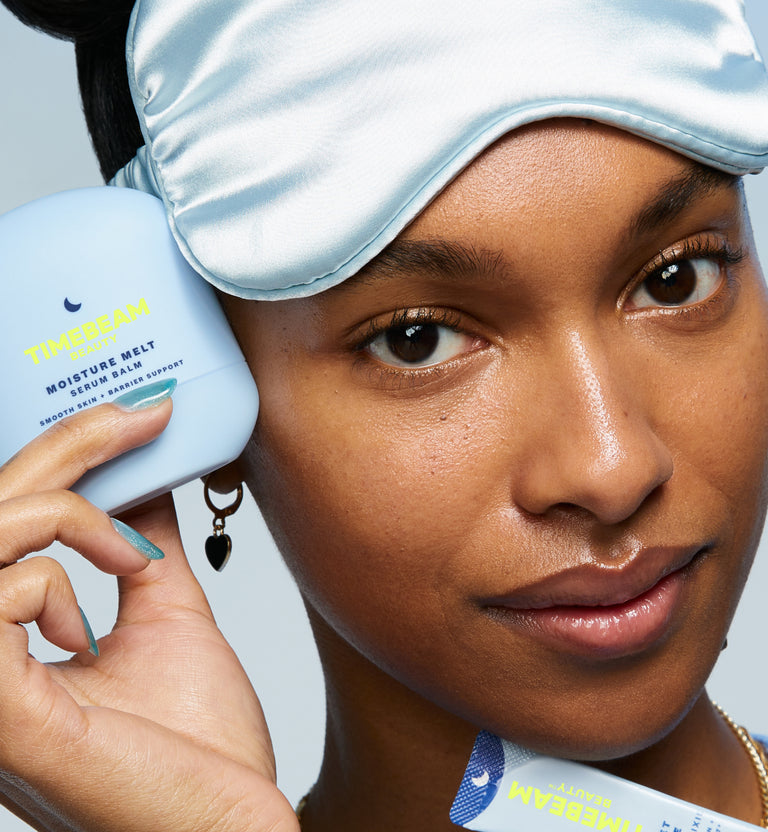 A woman with a sleeping mask on her head, holding TIMEBEAM skincare and supplements.