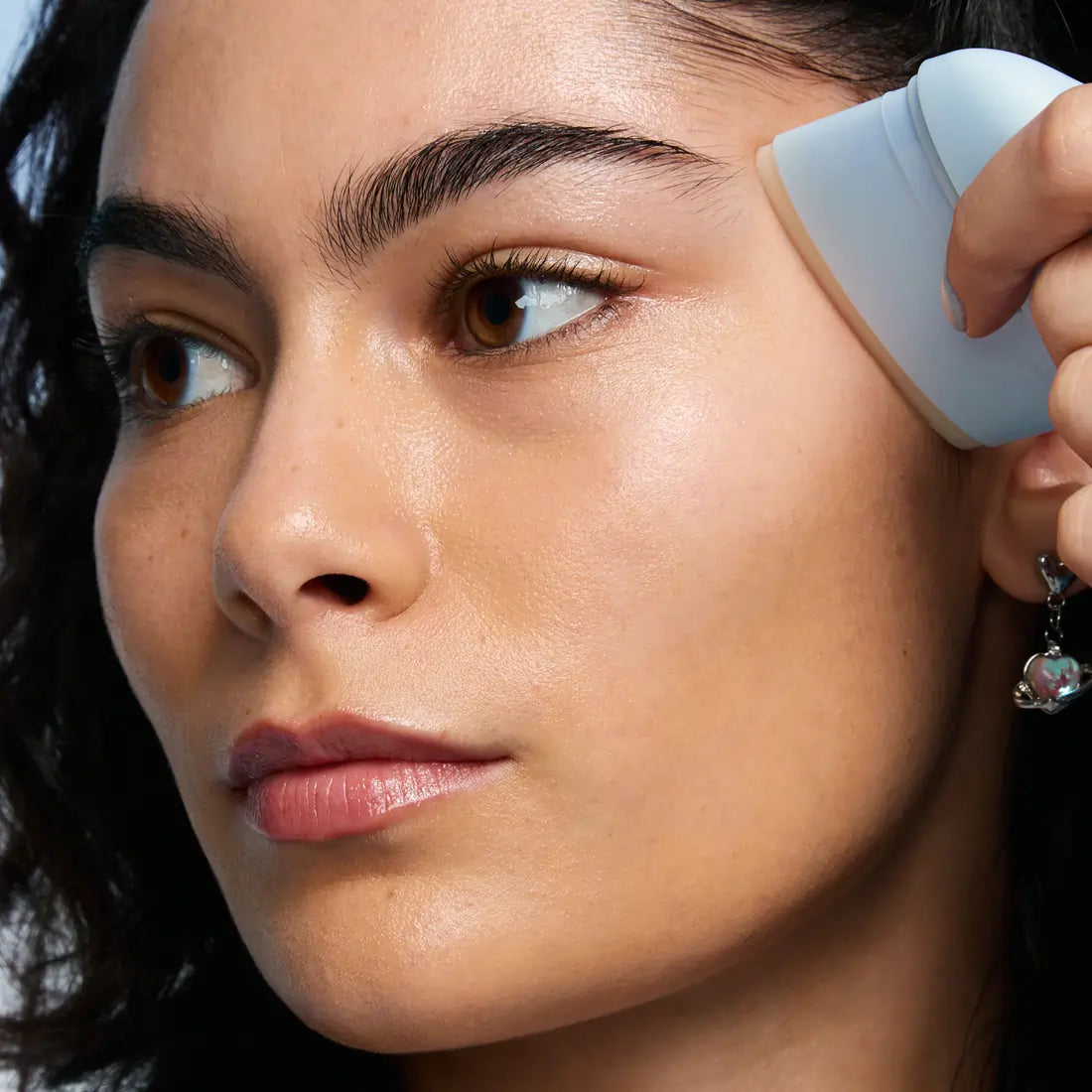 A woman applying TIMEBEAM Skinbeam Milky Serum to the side of her face.