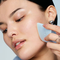 A smiling woman applying TIMEBEAM balm to her cheek.