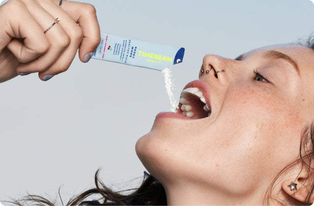A woman tilting the contents of an open pouch of TIMEBEAM supplements into her mouth