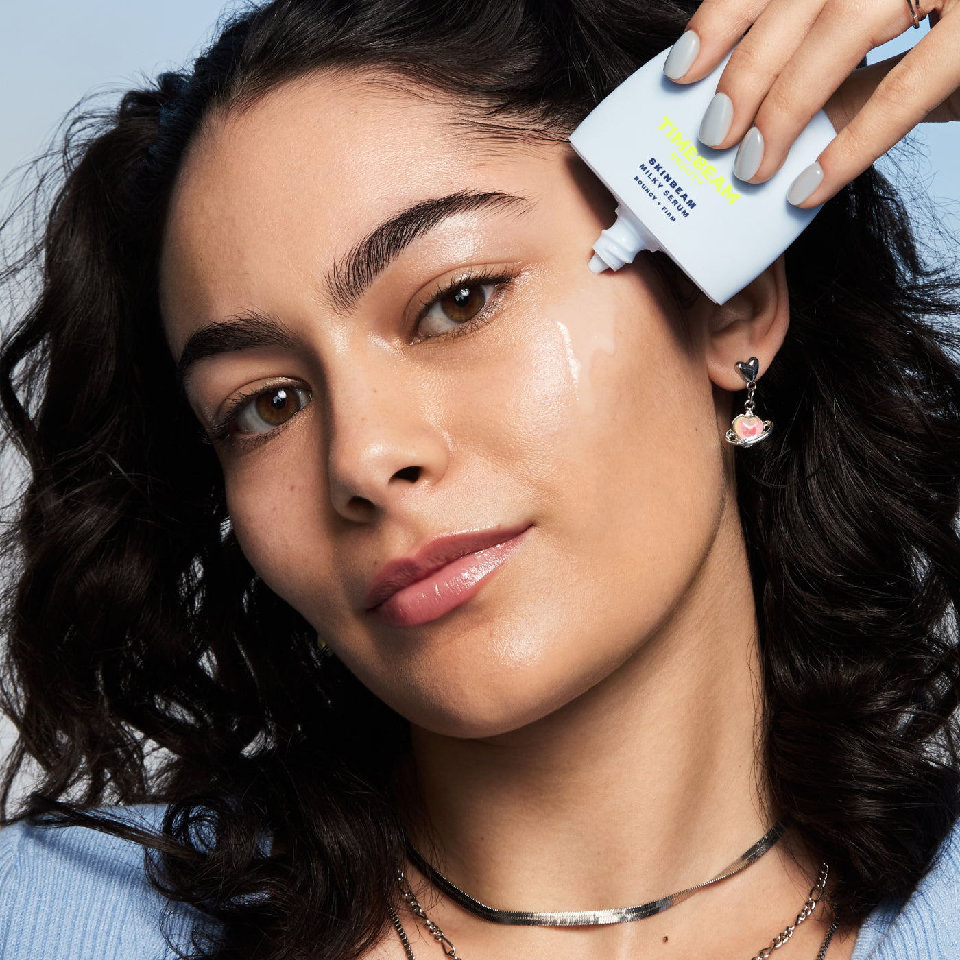 A woman applying TIMEBEAM Skinbeam Milky Serum to her cheek.