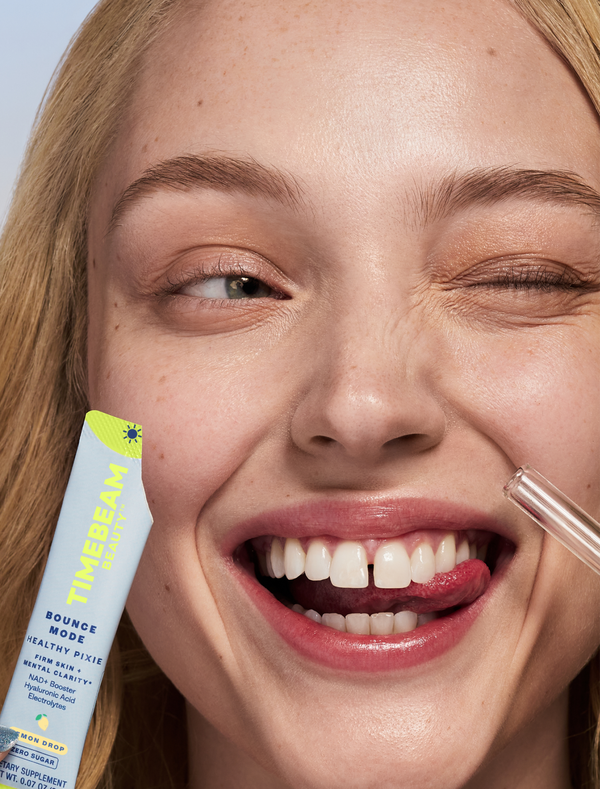 A smiling woman biting her tongue and winking while holding an open pouch of TIMEBEAM supplements.