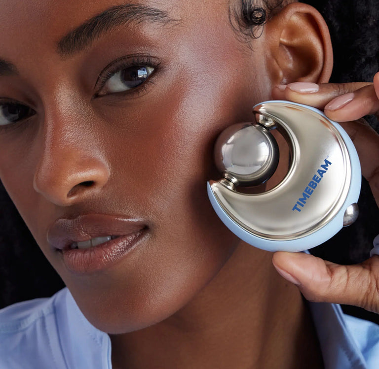Close-up of a woman holding a silver and light blue TIMEBEAM facial device against her cheek.