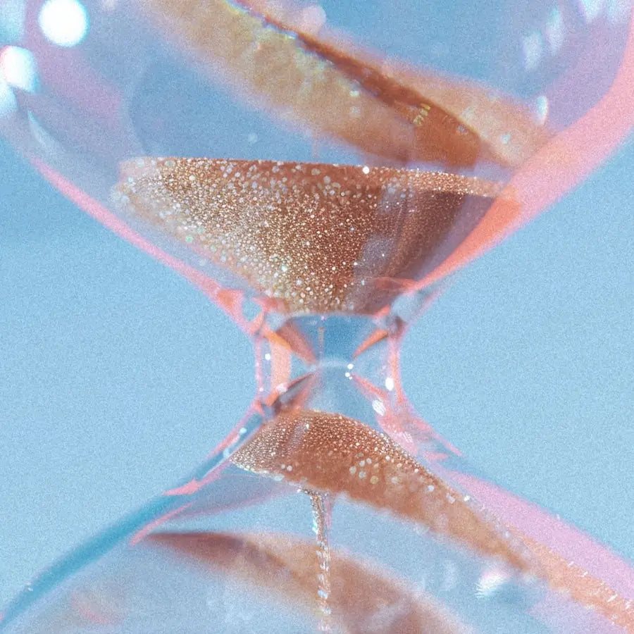 Close-up of an hourglass with glittering sand flowing from the upper chamber to the lower one.
