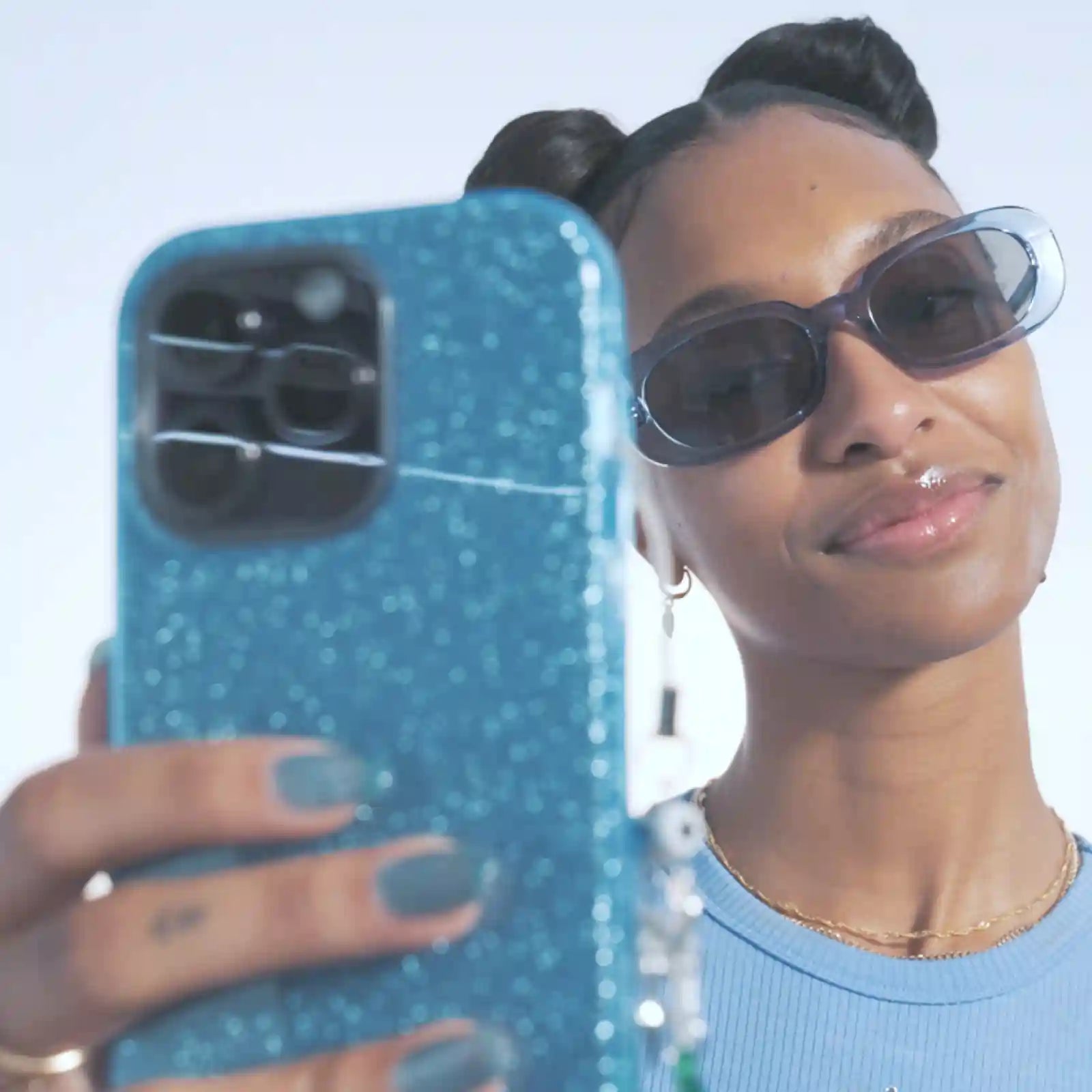 A woman in sunglasses holding a blue glittery phone case 