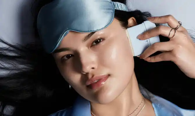 A woman with a sleeping mask on her forehead, applying a TIMEBEAM balm to the side of her face.