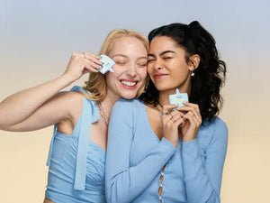 Two smiling women with their eyes closed, holding open bottles of TIMEBEAM skincare products.