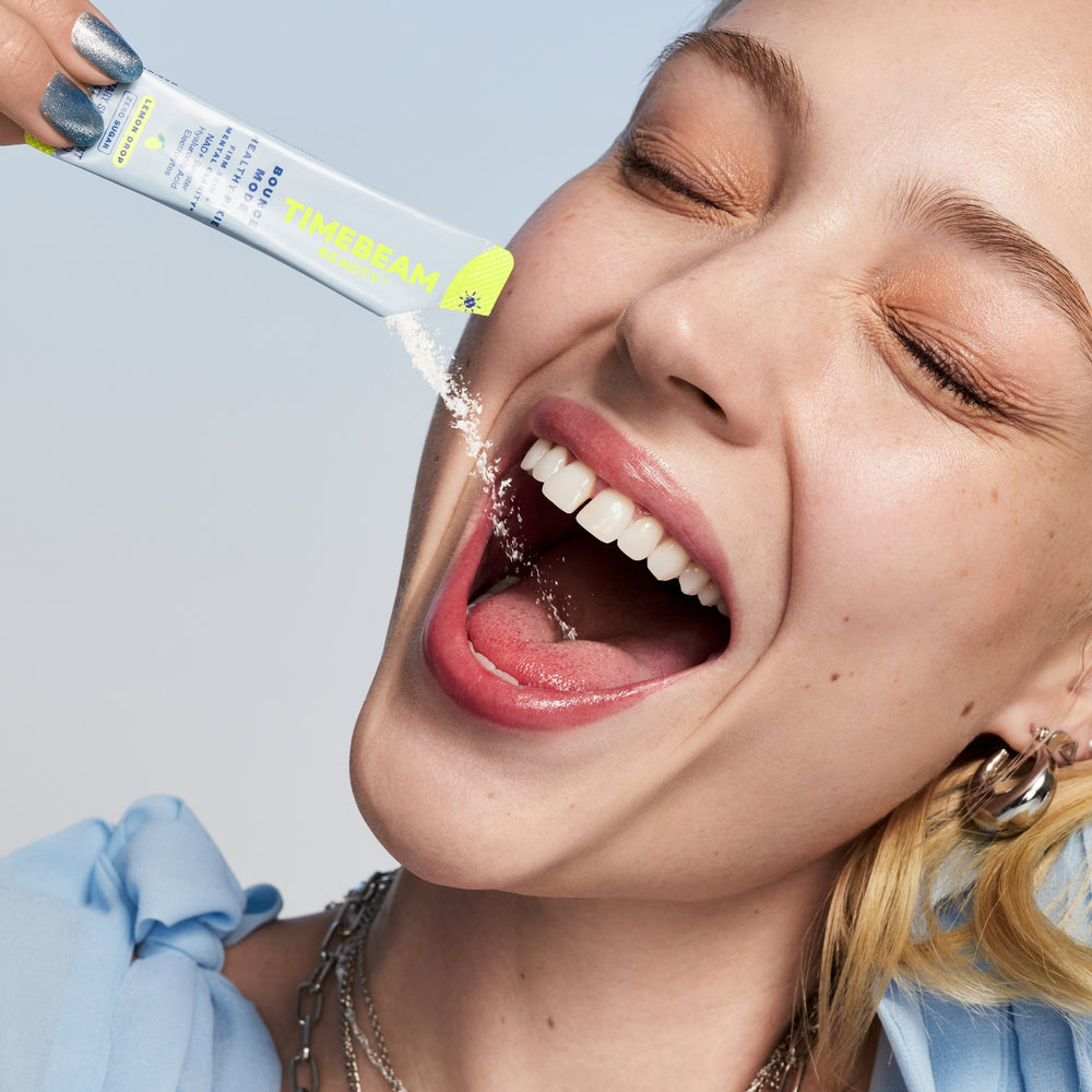 A woman tilting the contents of an open pouch of TIMEBEAM supplements into her mouth.