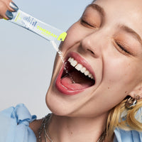 A woman tilting the contents of an open pouch of TIMEBEAM supplements into her mouth.
