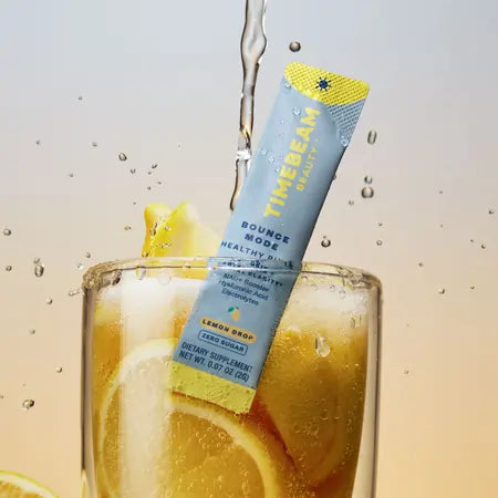 A TIMEBEAM supplement pouch in a glass filled with lemon slices, with water pouring on top.