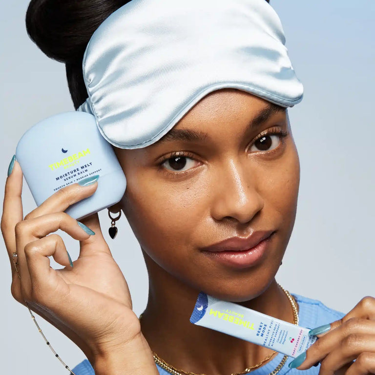A woman with a sleeping mask on her head, holding TIMEBEAM skincare and supplements.